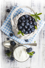 Blueberry basket and glass of yogurt on white wooden table
