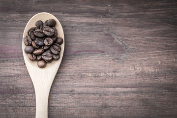 Coffee beans on spoon and wooden background