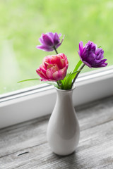 tulips in a white vase on a light wooden surface 