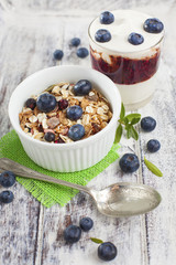 Bowl of muesli with fresh blueberries and glass of yogurt on whi
