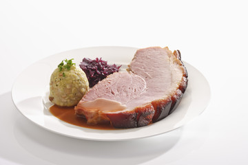 Eine Scheibe gebratenen Krustenbraten mit Semmelknödel, Blaukraut, Rotkohl, Sauce, teller
