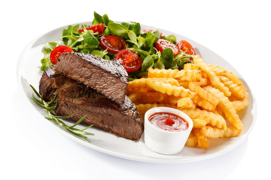Grilled steak, French fries and vegetables on white background 