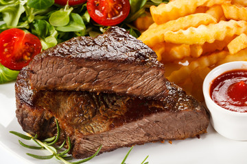 Grilled steak, French fries and vegetables on white background 