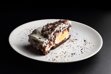 Piece of banana and chocolate cake on porcelain plate. Dark background