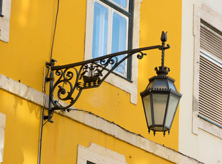  Black wrought iron wall lantern on a yellow wall.