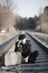 HOMBRE ELEGANTE JUNTO A LAS VIAS DEL TREN CON SOMBRERO Y MALETA