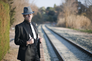 HOMBRE ELEGANTE JUNTO A LAS VIAS DEL TREN CON SOMBRERO Y MALETA