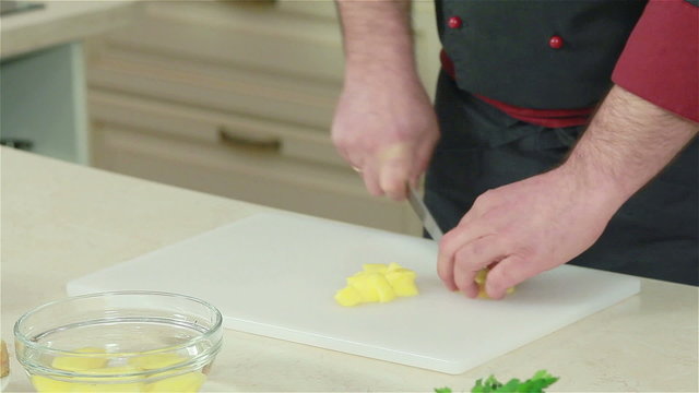 Frontal shot of chef cutting potato with a knife. Close-up