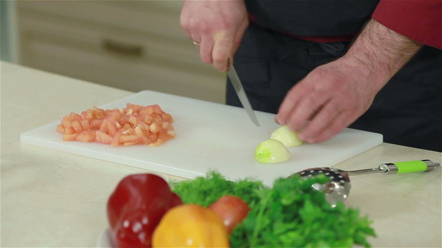 Frontal shot of chef cutting up onions and garlic on a board. Close-up