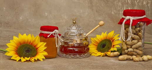 Country image with sunflowers, bee hive jar with honey and jar of peanuts against brown texture background
