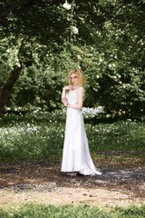 Beautiful young bride in white dress in summer green park
