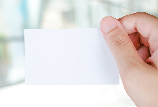 Blank name card in hand over blur office background