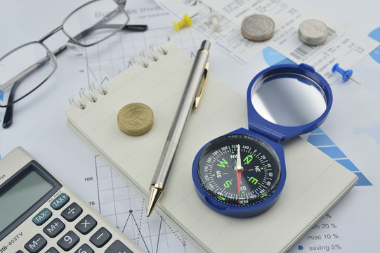 Compass, pen and coin on notebook, accounting background