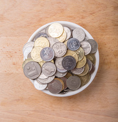 Malaysian coins in a white bowl over wooden surface