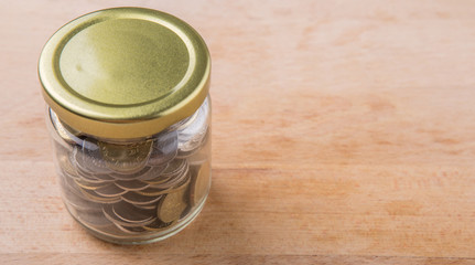 Malaysian coins in a mason jar over wooden background