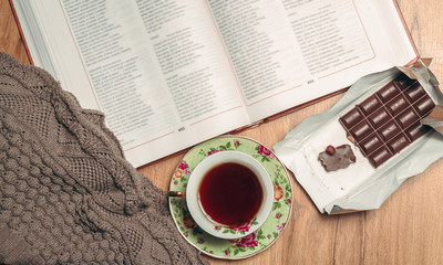 Still life. Warm, knitted sweater, a cup of hot tea, chocolate, a book on wooden background. top view