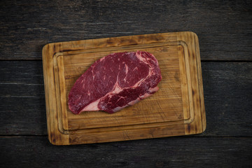 Raw ribeye beef steak overhead on wooden rustic board