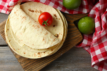 Stack of homemade whole wheat flour tortilla and vegetables on cutting board, on wooden table background
