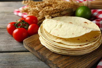 Stack of homemade whole wheat flour tortilla and vegetables on cutting board, on wooden table background