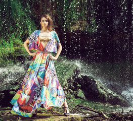 Young woman in a beautiful fashion dress posing outdoor. Waterfall background.