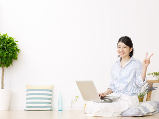 Fototapeta premium 部屋でノートパソコンを使う女性 ピースサイン