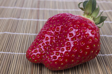 one ripe strawberry on a wooden mat