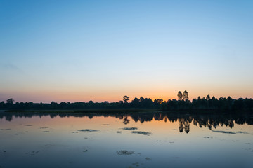 Naklejka premium Beautiful sunrise over calm lake. Colorful and vibrant landscape of lake shore. Tranquil landscape useful as background