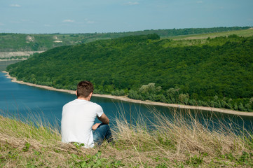 Young man sitting on a top of a mountain viewing wide river