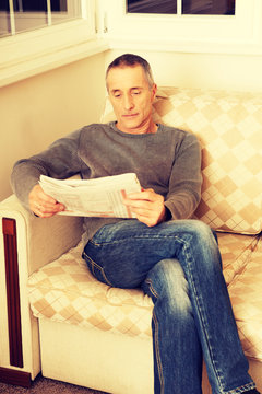 Middle-aged man reading newspaper at home