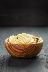 rippled organic chips in wood bowl on wooden table with copy