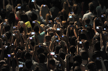 Excited youngsters attending a show, applauding and taking videos vith cell phones