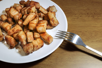Pork fried with salt which put on a white dish and fork is beside
