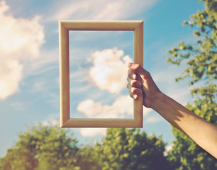 Hand holding a wooden frame on cloud background. Care, safety, m