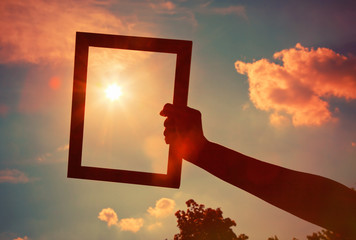 Hand holding a wooden frame on sunrise sky background. Care, saf