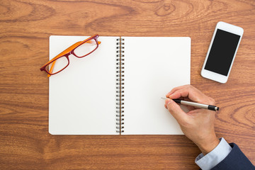 Businessman hand with a pen writting blank notebook on wooden ba