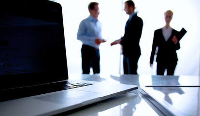 Laptop  computer on  desk , three businesspeople standing in the
