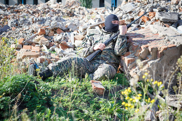 Military camouflage with a rifle on a background of bombed buildings.