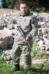 Military camouflage with a rifle on a background of bombed buildings.