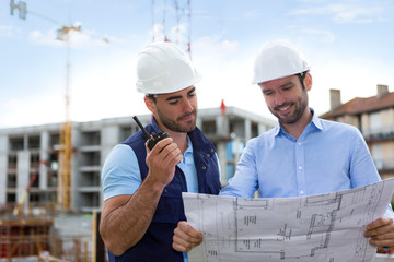 Engineer and worker watching blueprint on construction site