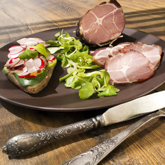 Crude, dried, organic gammon ham with sandwich and salad on plate on wooden table