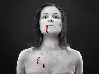Zakrwawiona kobieta pomalowana na biało na ciemnym tle