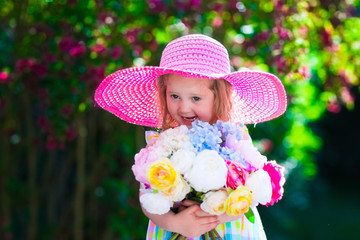 Little girl in a hat in blooming summer garden