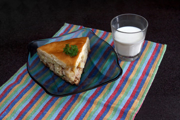 Chicken and potato pie segment with glass of milkt against black marble background © yarlander