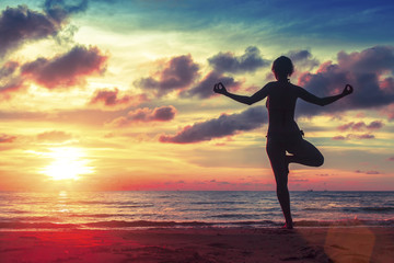 Silhouette  woman practicing yoga on the beach at surrealistic sunset. 