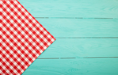 Red plaid tablecloth on blue wooden background. Top view
