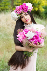 Fototapeta premium Beautiful woman with long beautiful hair in a pink dress posing with a bouquet and wreath of peonies. Bride 