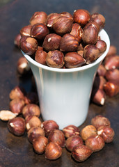 Raw hazelnuts, no shell, in a white cup on rustic brown background.