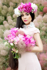 Beautiful woman with long beautiful hair in a pink dress posing with a bouquet and wreath of peonies. Bride
