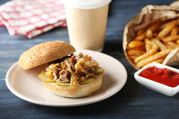 Tasty burger and french fries on plate, on wooden table background. Unhealthy food concept