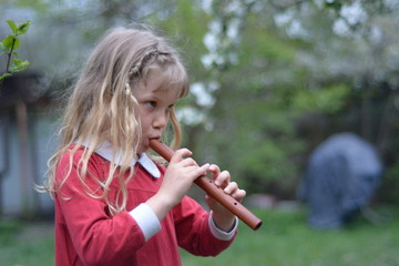 White girl in a red sundress, playing the flute on a green background © rimm7616